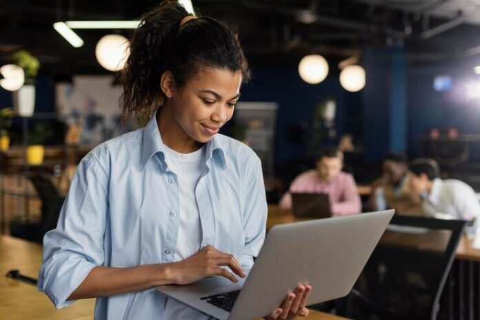 mulher-sorridente-segurando-um-laptop-no-escritorio-e-trabalhando-em-projetos-de-tecnico-administrat.jpeg